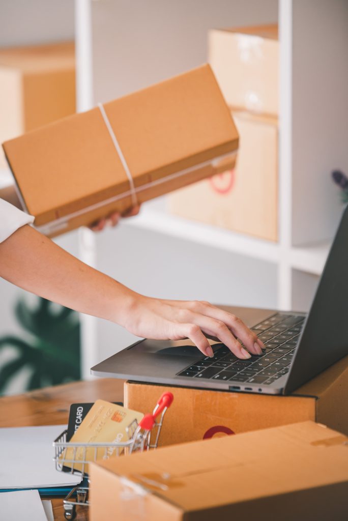 woman holding box and typing on laptop keyboard