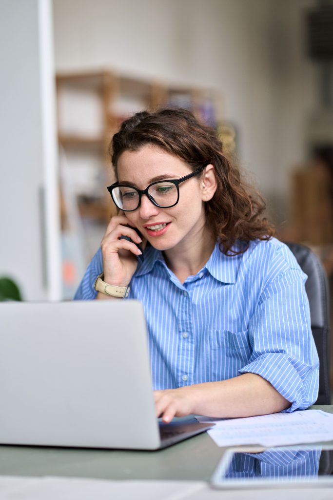 woman with glasses on laptop talking on the phone