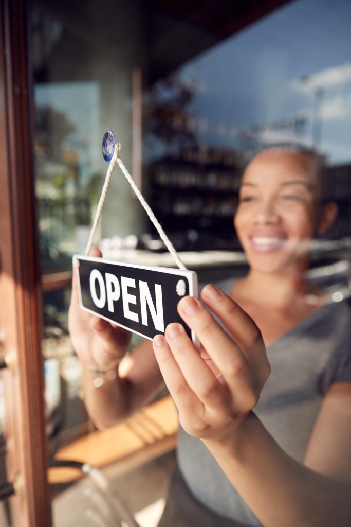 woman in storefront flipping open sign on door