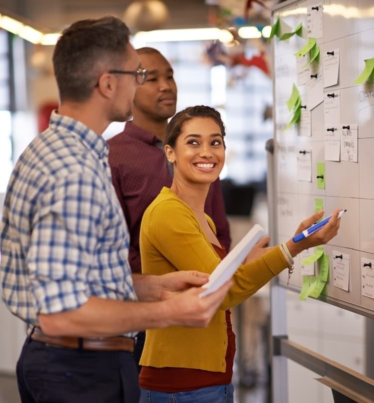 A close knit team working together to brainstorm a campaign strategy for a client. A smiling women holding an expo marker looking at her coworker.